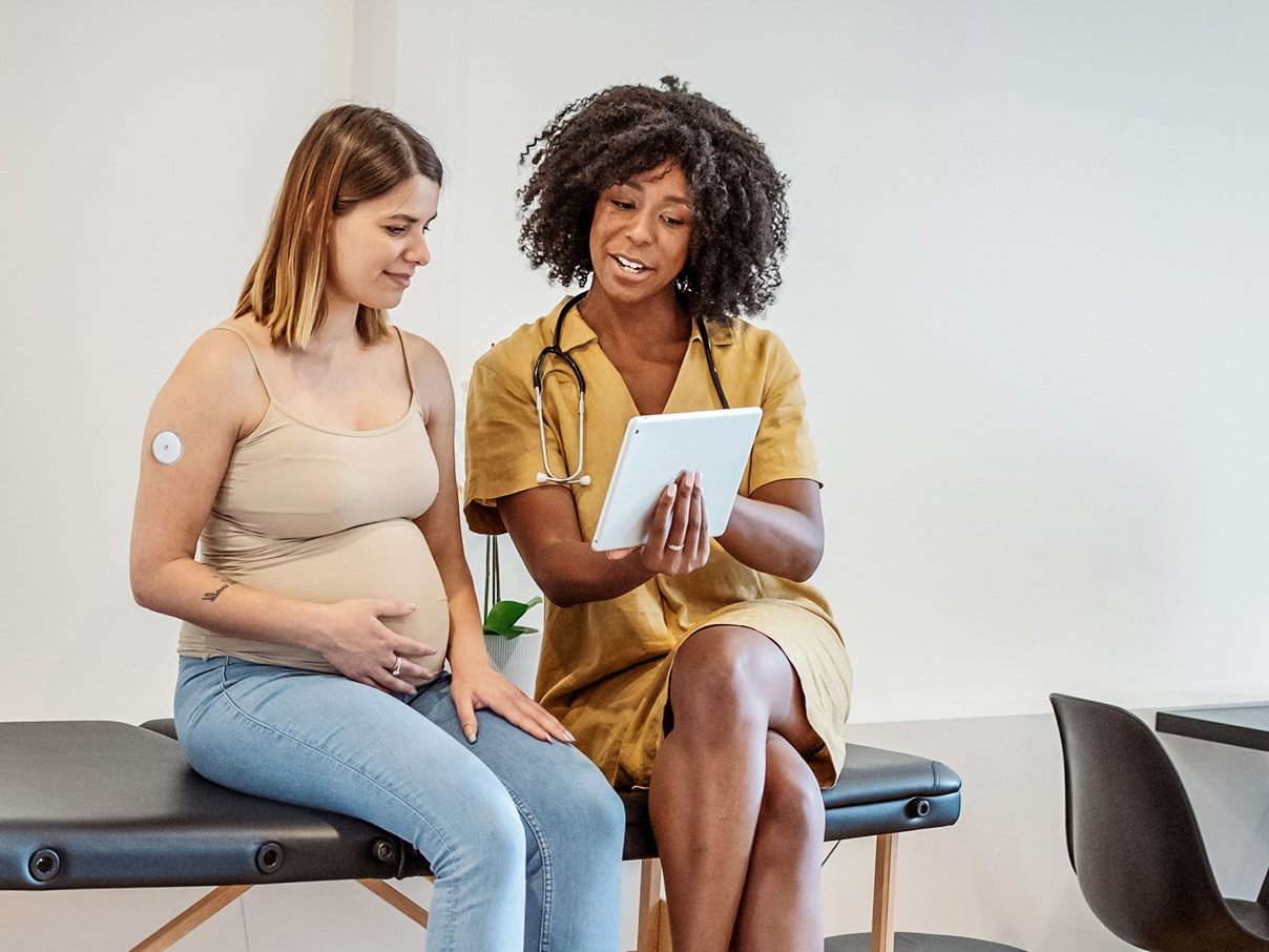 Clinician reviewing glucose data on a tablet with a pregnant patient wearing a CGM